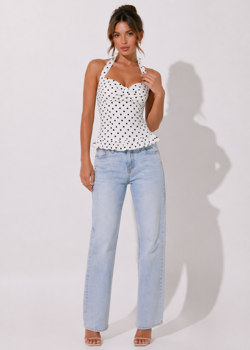 Woman wearing a polka dot top and light blue jeans against a white background