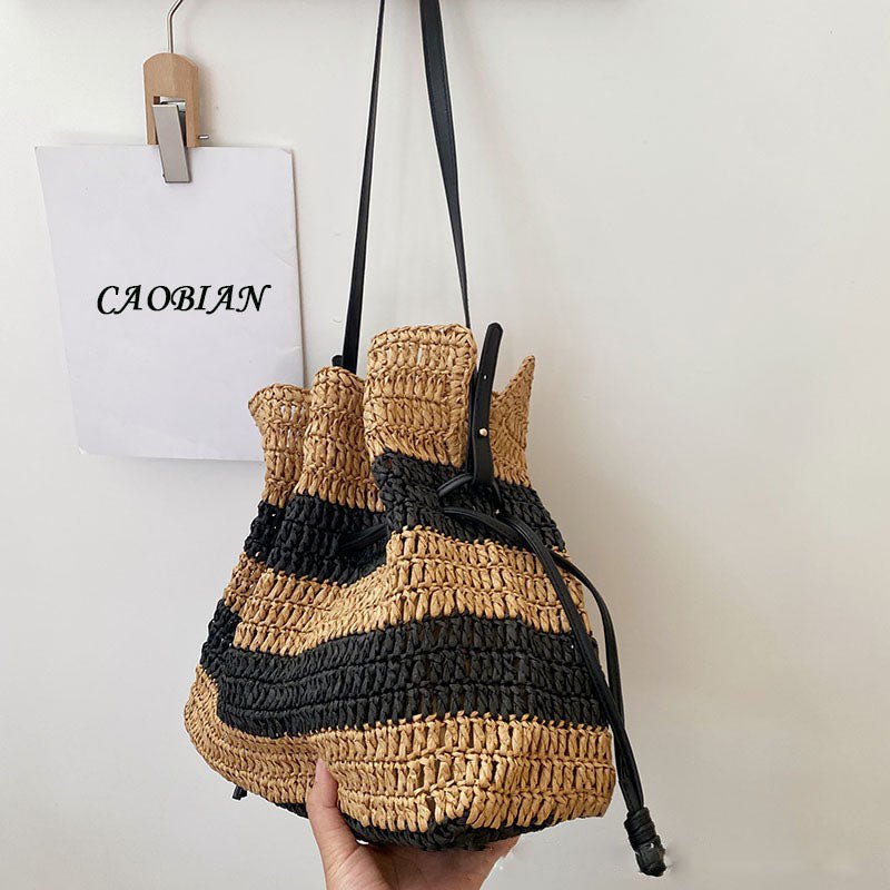 Hand holding the Calla striped woven drawstring bag by its black shoulder strap