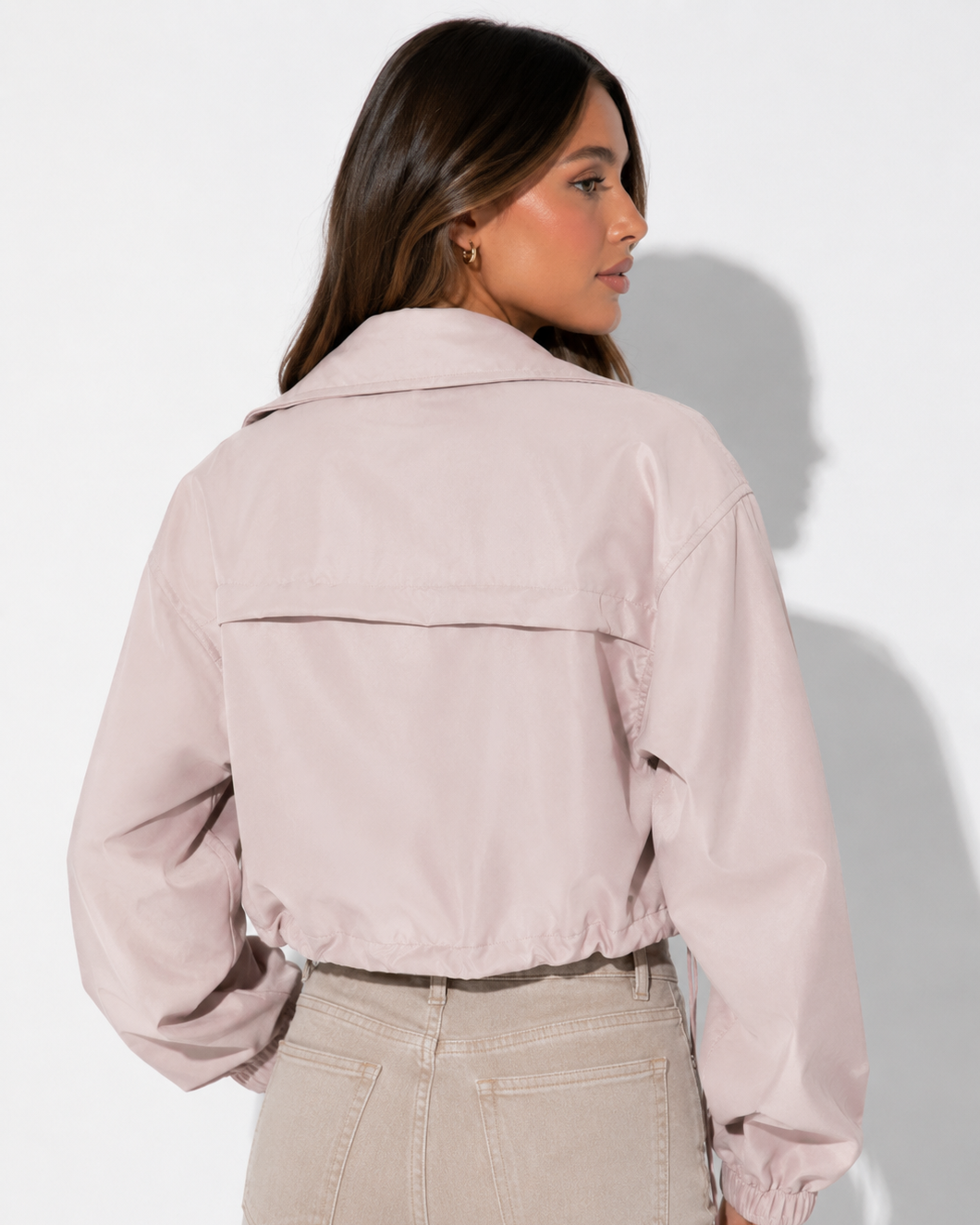 Woman wearing a light pink jacket and beige pants against a white background