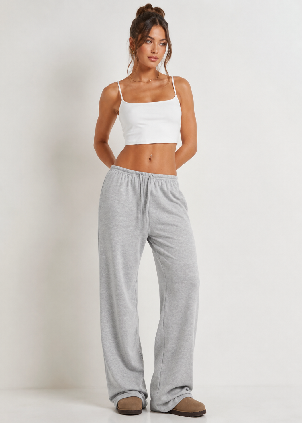 Woman wearing a white tank top and gray sweatpants on a plain background