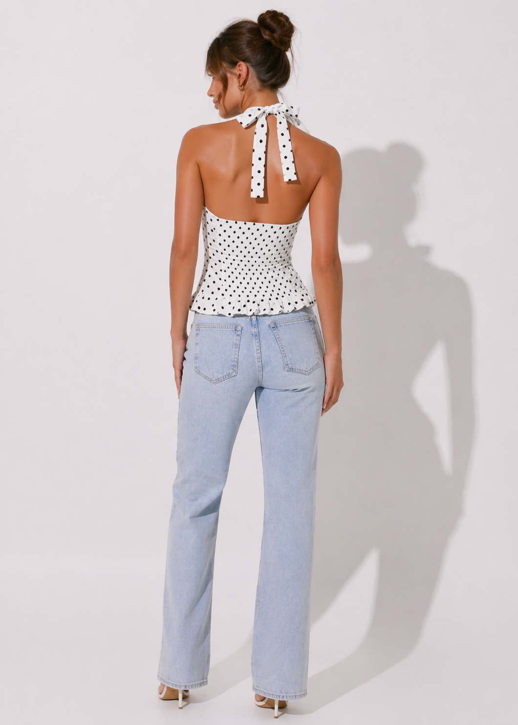 Woman wearing a polka dot halter top and light blue jeans on a white background