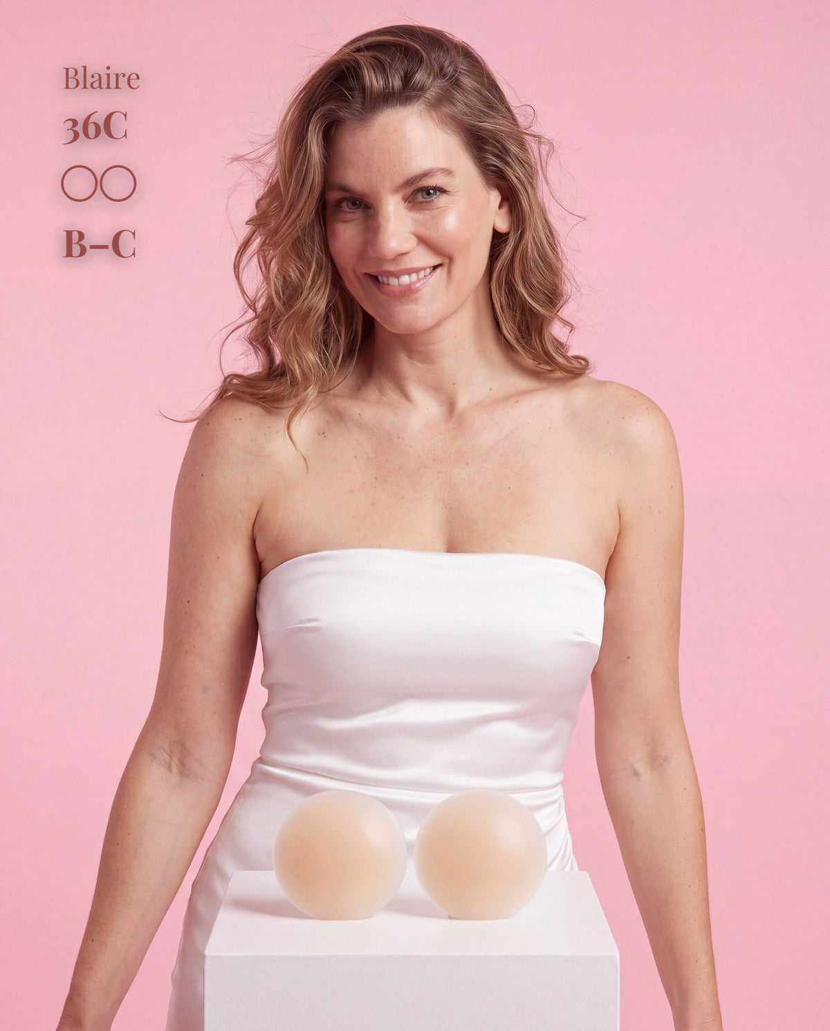 Model in a white strapless top holding Sticky Boobs silicone covers, size B-C