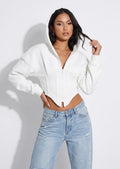 Model wearing the white cropped zip corset hoodie with light wash jeans, angled view