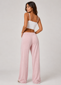 Woman wearing a white top and pink pants on a plain background
