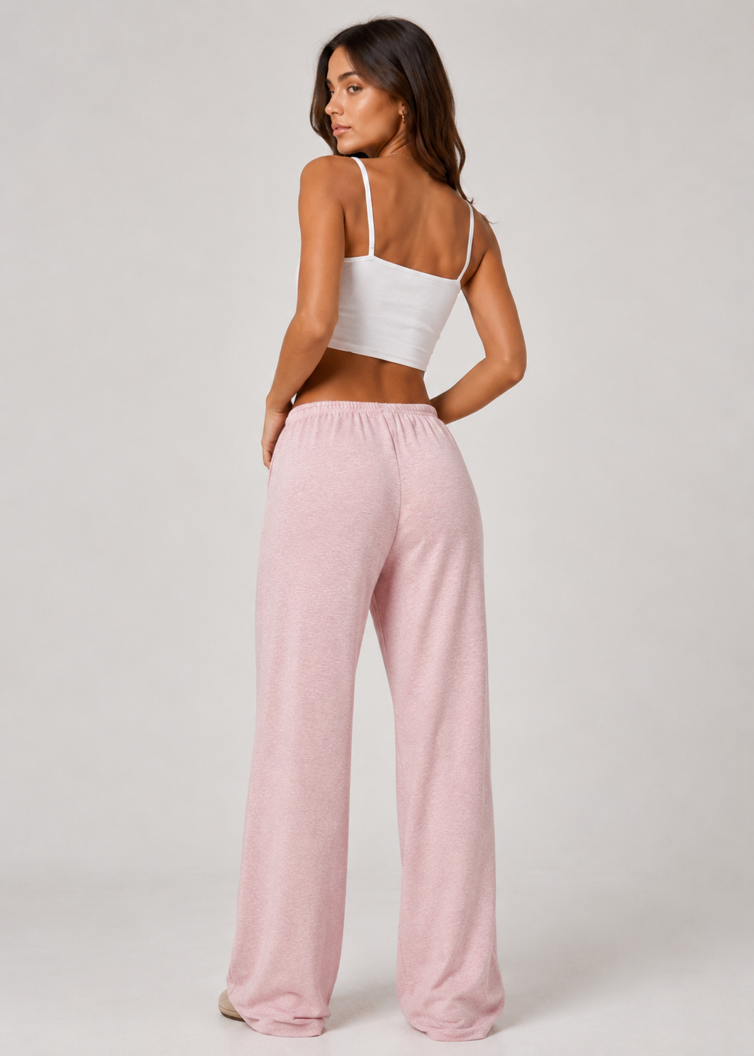 Woman wearing a white top and pink pants on a plain background