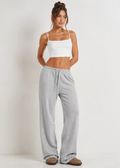 Woman wearing a white tank top and gray sweatpants on a plain background