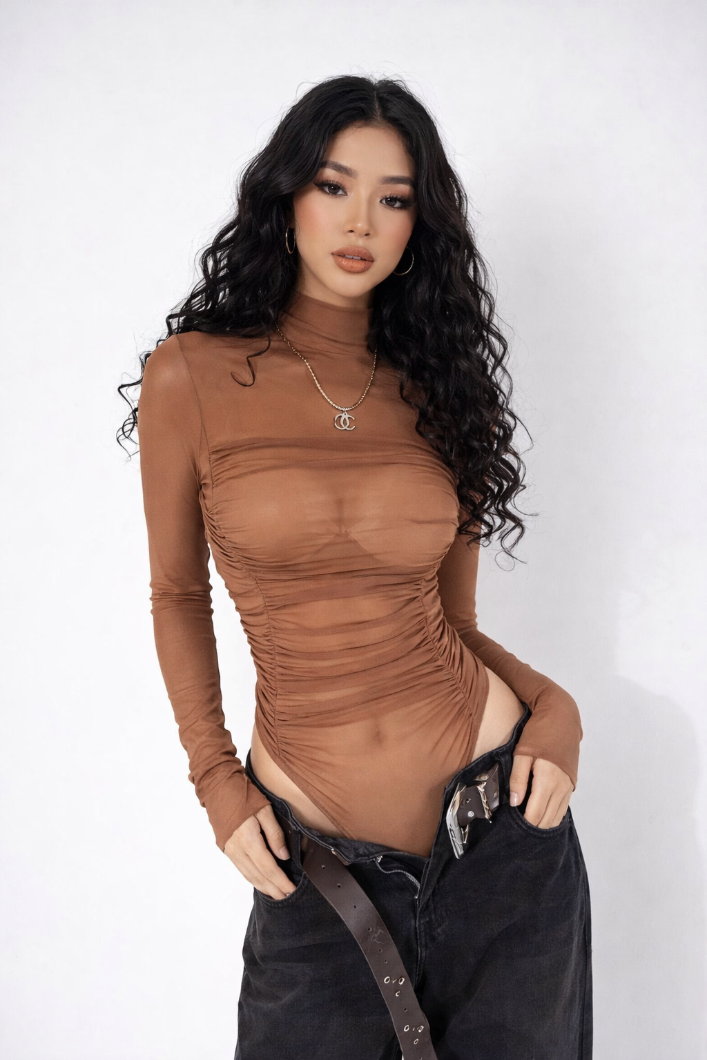Woman wearing a brown long-sleeve top and black pants against a white background