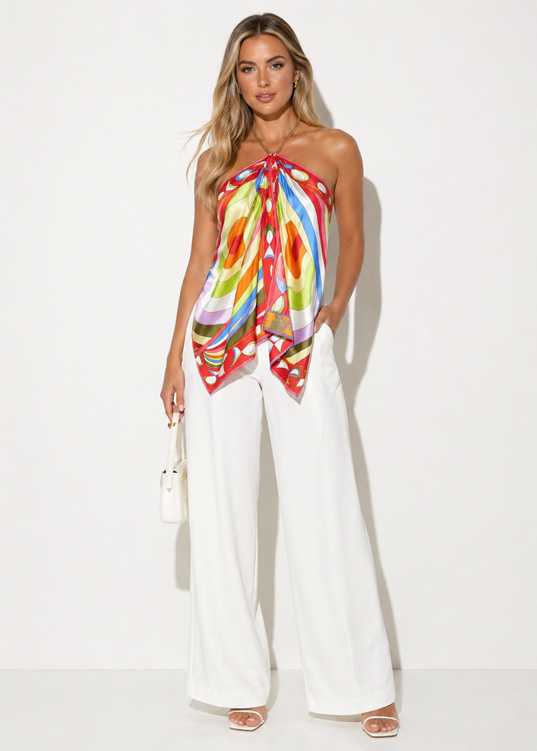 Woman wearing a colorful halter top and white pants on a white background