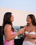 Two women laughing at a rooftop party in strapless and backless dresses