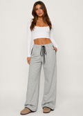 Woman wearing a white long-sleeve crop top and gray sweatpants on a white background